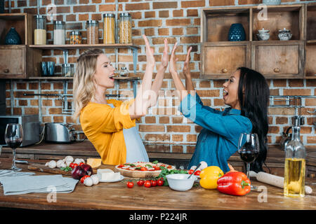 Fröhlicher junger miltiehnic Frauen hoch fünf beim Kochen in der Küche Stockfoto