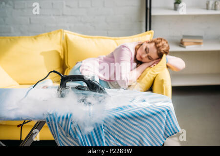 Bügeleisen Brennen auf Shirt, während Frau schlafend auf dem Sofa zu Hause Stockfoto