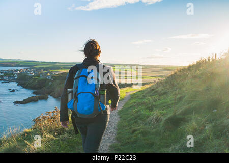 Foto einer aktiven Frau, die auf einem Küstenweg in Richtung Sonne wandert, der zum Dorf St Abbs auf der Ostseite Schottlands führt Stockfoto