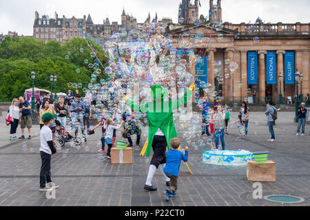 Männliche street Entertainer in Edinburgh, gekleidet in einem bunten Kostüm unterhalten Kinder und Erwachsene mit viel Seife Luftblasen in den Himmel. Stockfoto