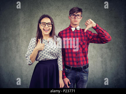 Junge stilvollen Mann mit Daumen nach unten stehend mit optimistischen Mädchen mit Daumen nach oben an der Kamera schaut. Stockfoto