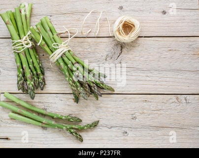 Zwei Bündel von frischem Grün bio Spargel und eine Rolle der Thread auf einem alten Holztisch. Selektive konzentrieren. Ansicht von oben und Platz kopieren Stockfoto