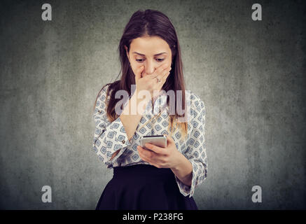 Junge Frau, die den Mund vor Erstaunen beim Lesen der Nachricht auf dem Smartphone suchen wie betäubt. Stockfoto