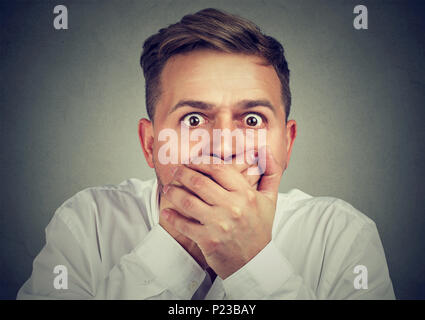 Portrait des jungen Mannes in den Mund mit beiden Händen in Angst ausdrücklich an Kamera schaut. Stockfoto