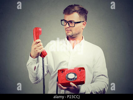 Junger Mann in Brillen mit roten altmodische Telefon bei der Suche in großen Erstaunen. Stockfoto