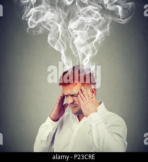 Konzeptionelle Schuß von Mann, Hände auf Tempel und Suchen mit Rauch aus Kopf frustriert. Stockfoto