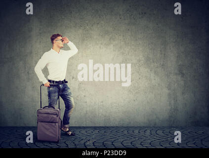 Junge legerer Mann stehend mit Gepäck und die Hand vor Augen, wenn Sie auf der Suche. Stockfoto