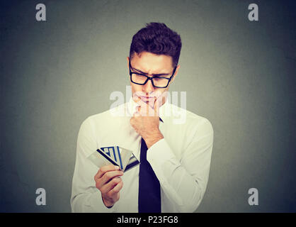 Nachdenklicher Mann mit vielen verschiedenen Kreditinstituten Treuerabatt Karten auf grauen Hintergrund. Stockfoto