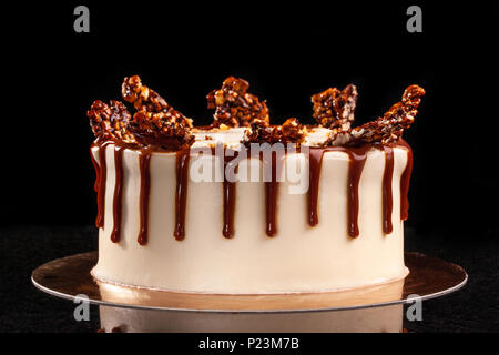 Runde weiße Kuchen mit Karamell und Schokolade Puffreis auf ein rundes Tablett auf schwarzem Hintergrund. Noch immer leben Stockfoto