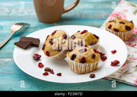 Vanille Muffins mit getrockneten Kirschen auf den weißen und blauen Holzmöbeln rustikal Tisch. Schokolade Stockfoto