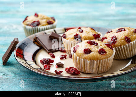 Vanille Muffins mit getrockneten Kirschen auf den weißen und blauen Holzmöbeln rustikal Tisch. Schokolade Stockfoto
