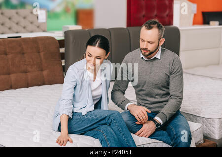 Portrait von Paar Sitzen auf Matratzen, während Ware zusammen die Wahl in Möbelhaus Stockfoto