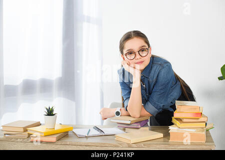 Adorable jugendliche Kind ruht das Kinn auf die Hand am Tisch mit Büchern zu Hause Stockfoto