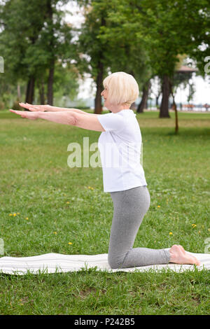 Ältere Frau Yoga auf der Matte auf grünen Rasen in Park Stockfoto