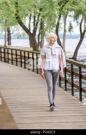 Lächelnde ältere Frau zu Fuß auf Holz- Pfad in Park Stockfoto