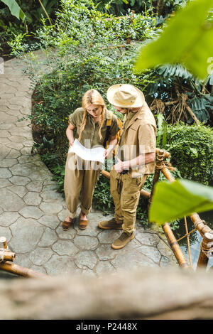Hohe Betrachtungswinkel und der schöne junge Paar in Safari Anzüge mit Karte im Dschungel Stockfoto