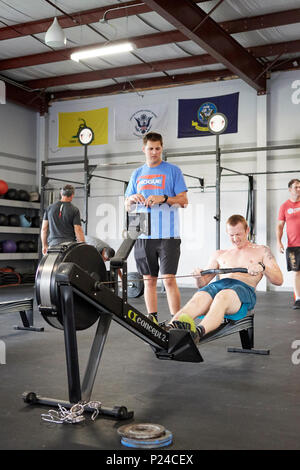 Mann oder Mann in einem CrossFit Fitness Challenge Wettbewerb mit einem Rudergerät bis zur Erschöpfung in einem Fitnessstudio in Montgomery Alabama, USA konkurrieren. Stockfoto