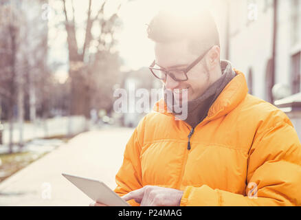 Junge legerer Mann in Brillen mit Tablette während draußen in den sonnigen Wintertag. Stockfoto