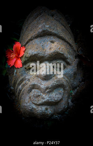 Alte balinesischer Stein mit einem roten Hibiskus Blume hinter dem Ohr, Ubud, Bali, April, 14 2018 Stockfoto