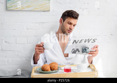 Schöner Mann im Bademantel lesen Zeitung beim Frühstück mit Kaffee Stockfoto