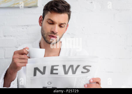 Junger Mann mit Tasse Kaffee lesen Zeitung am Morgen Stockfoto