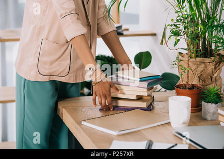 Zugeschnittenes Bild des afrikanischen amerikanischen Geschäftsfrau, Bücher auf dem Tisch im Büro Stockfoto