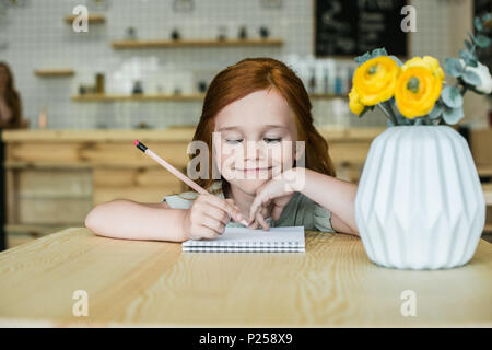 Adorable lächelnd rothaarige Mädchen Zeichnen mit Bleistift im Cafe Stockfoto