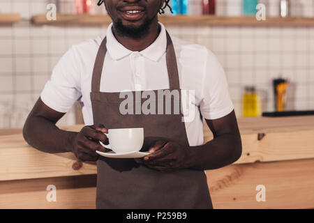 Ansicht der afrikanischen amerikanischen Barista in Schürze holding Tasse Kaffee im Stehen an der Theke 7/8 Stockfoto