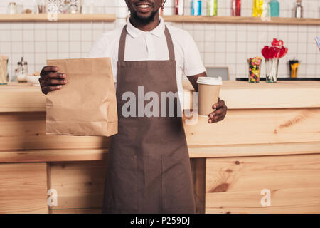 Ansicht der afrikanischen amerikanischen Barista holding Einweg Tasse Kaffee und kraft Paket am Tresen 7/8 Stockfoto