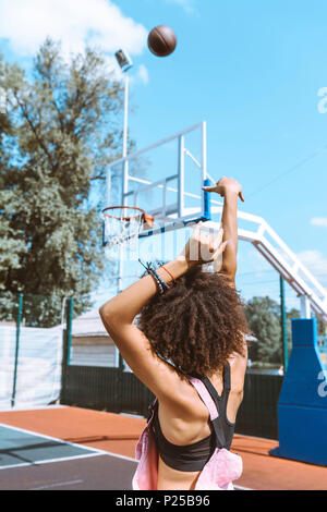 Ansicht von hinten erschossen Der junge Afrikaner - amerikanische Frau im Sport-BH und Rosa overalls Werfen eines Basketball Ball Stockfoto