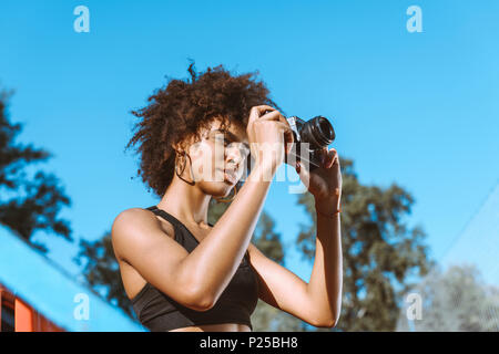 Junge afrikanische amerikanische Frau im Sport-BH sitzt in den Zuschauertribünen mit Kamera Stockfoto