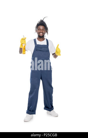 Lächelnd african american Cleaner in Uniform mit Waschmittel, Daumen hoch, isoliert auf weißem Stockfoto
