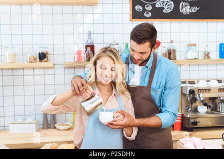 Lächelnden jungen Paar in Schürzen Kaffee zusammen im Cafe Stockfoto