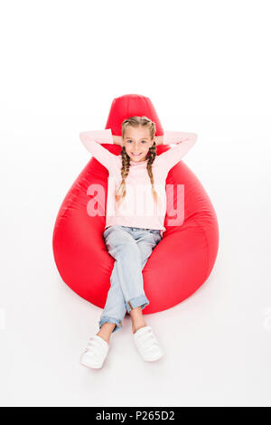 Junge glückliches Kind ruht auf einem roten Bean Bag mit Arme hinter Kopf, isoliert auf weißem Stockfoto