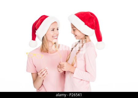 Glückliche Mutter mit Tochter in santa Hüte holding Karton Party Brille auf Weihnachten, isoliert auf weißem Stockfoto