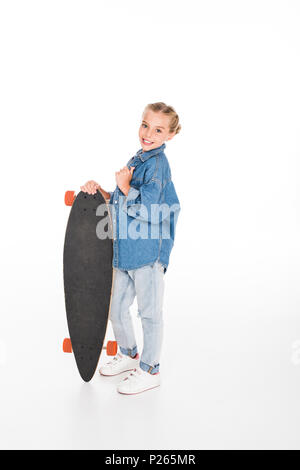 Kleines Kind in überdimensionalen Jeanshemd posiert mit einem Longboard, isoliert auf weißem Stockfoto