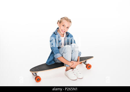 Kleines Kind in überdimensionalen Jeanshemd sitzen auf einem longboard, isoliert auf weißem Stockfoto