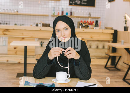 Junge muslimische Frau mit gebetsperlen allein sitzen im Cafe Stockfoto