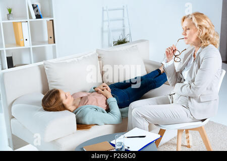 Im mittleren Alter Psychologe holding Brillen und Blick auf junge weibliche Patient auf Behandlungstisch Stockfoto