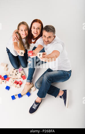 Junge Mutter, Tochter und Vater zeigen Alphabet Blöcke mit Buchstaben m, d und f, isoliert auf weißem Stockfoto