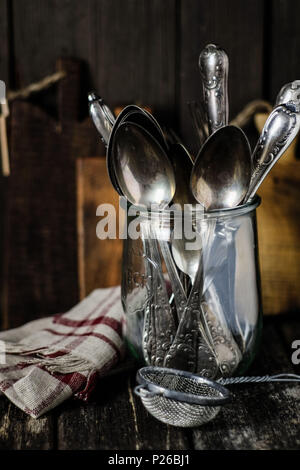 Stillleben mit Vintage Küchengeräte: altes Silberbesteck in ein Glas, alte Sieb, Leinen und Holz Stockfoto