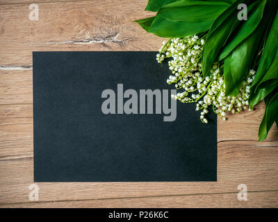 Bouquet of lilies of the valley on a wooden background and an empty piece of black paper. Stockfoto