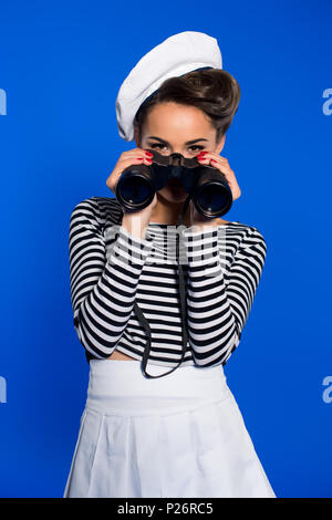 Attraktive junge Frau in retro Bekleidung mit Fernglas isoliert auf Blau Stockfoto