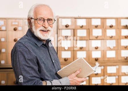 Lächelnd älterer männlichen Archivar holding Buch und Kamera Stockfoto