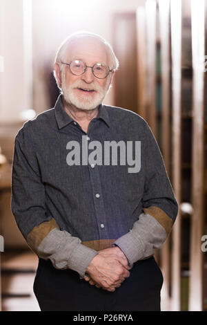 Happy graue Haare Bibliothekar stehen zwischen Regalen Stockfoto
