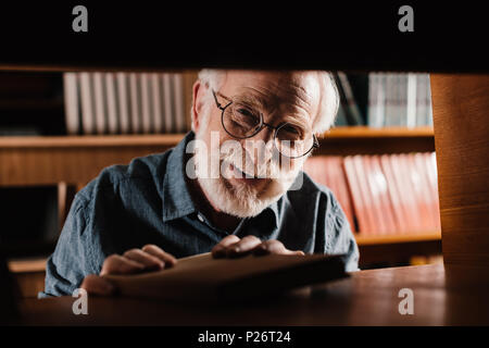 Lächelnd graue Haare Bibliothekar auf Kamera über Haltbarkeit Stockfoto