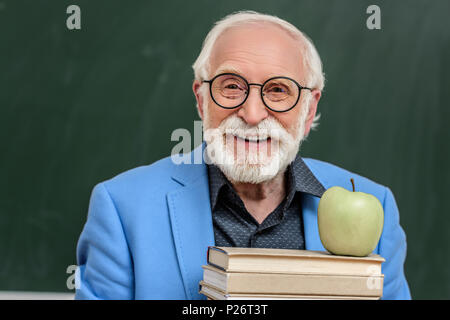 Lächelnd graue Haare professor Holding der Bücher mit Apple auf der Oberseite des Zusatzsteuerventilblocks Stockfoto