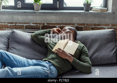 Porträt der jungen afrikanischen amerikanischen Mann mit Buch schlafend auf dem Sofa zu Hause Stockfoto