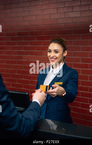 Junge happy Hotel Rezeptionistin, die Kreditkarte des Kunden Stockfoto