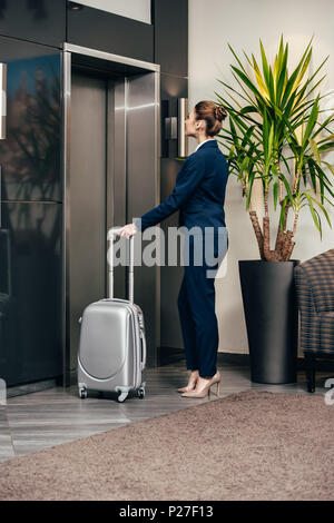 Junge attraktive Geschäftsfrau für Aufzug im Hotel wartet mit Gepäck Stockfoto